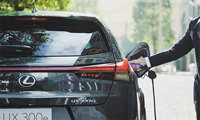 A man dressed in a suit stretches out his arm to connect the charging cable on a Lexus UX 300e