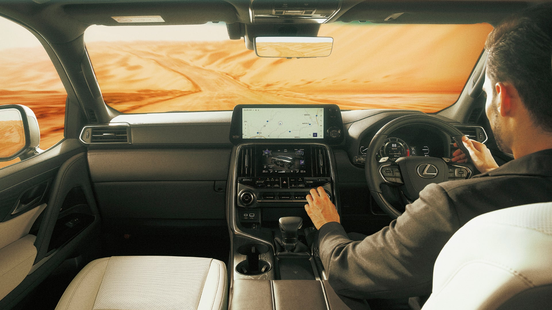 A man sits behind the wheel of an LX - the stretch ahead is desert. He is reaching for the dual display, located within the Tazuna cockpit.