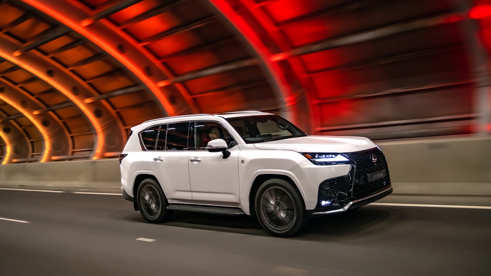 Lexus LX drives under a coloured, lit up city highway.