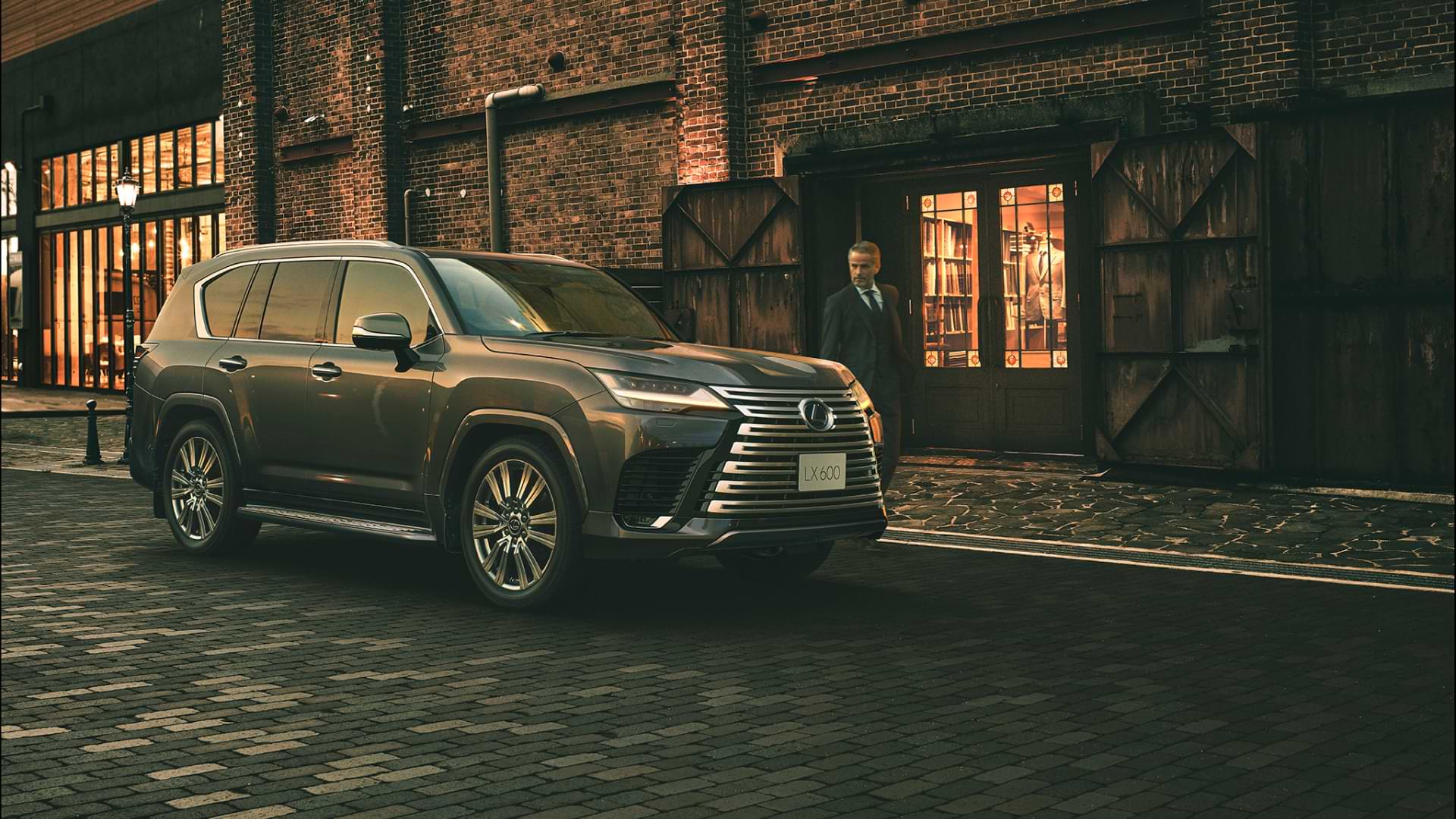 LX sitting parked on a cobbled stone street, a well-dressed man stands next to it.