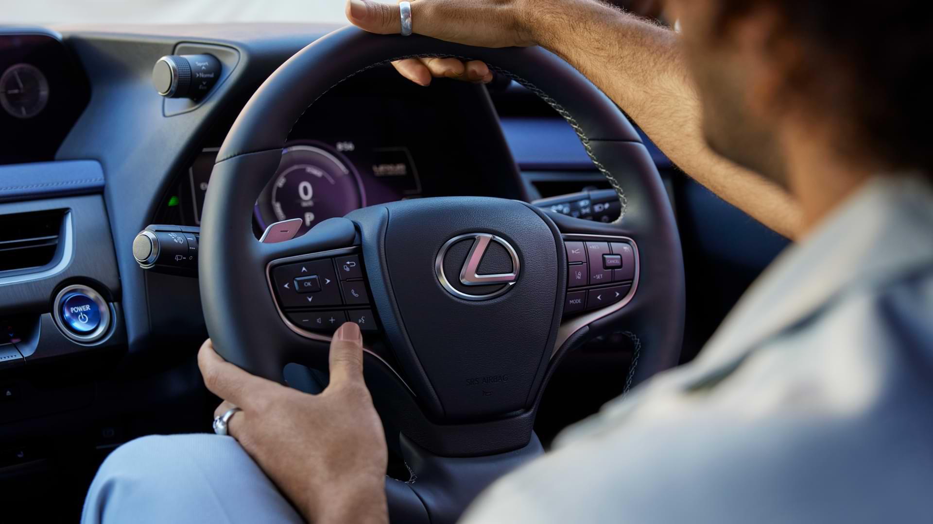 Man holds the steering wheel of the UX 300e, the driver display is illuminated.