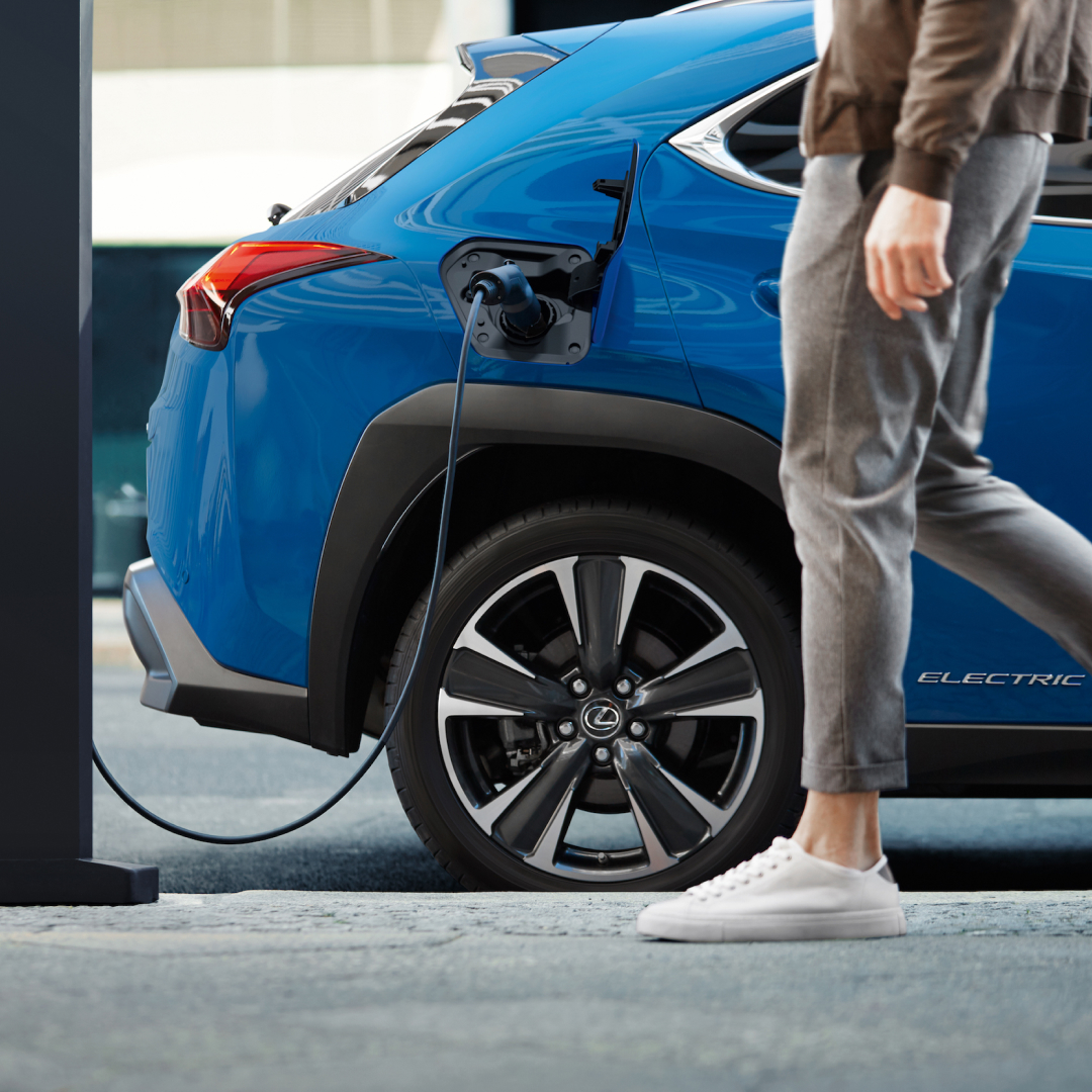 A man's leg is in front of a charging, blue UX 300e. He is walking to the charger.