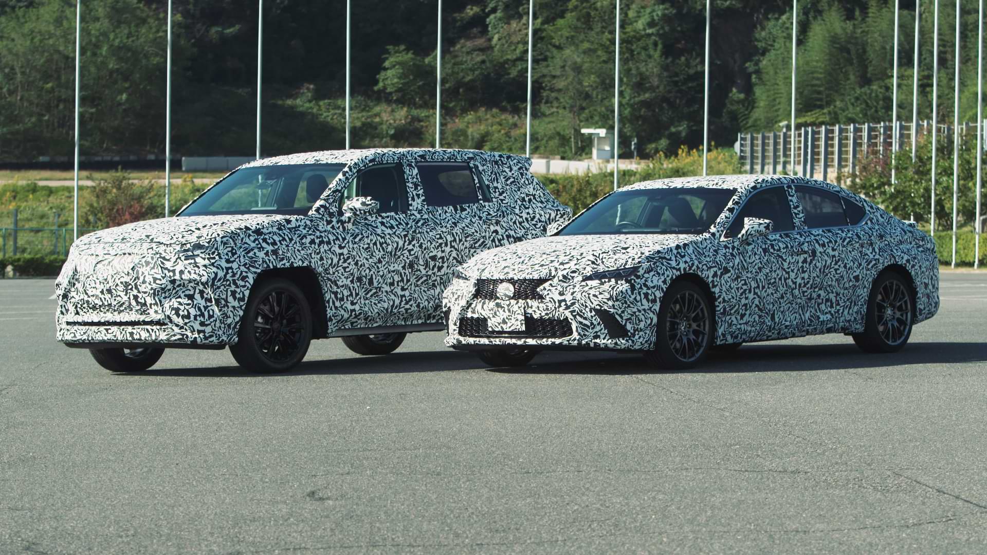 Black and white speckles Lexus BEV and HEV prototypes sit on a concrete road.