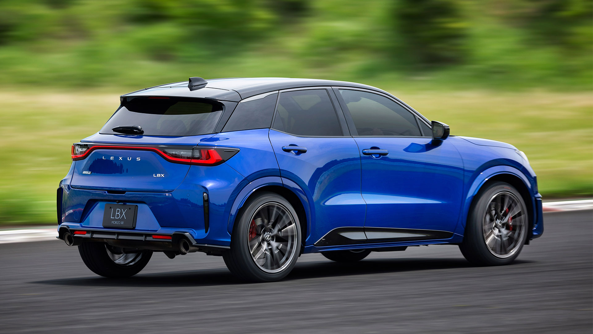 A blue Lexus LBX Morizo RR drives along a road with trees in the background